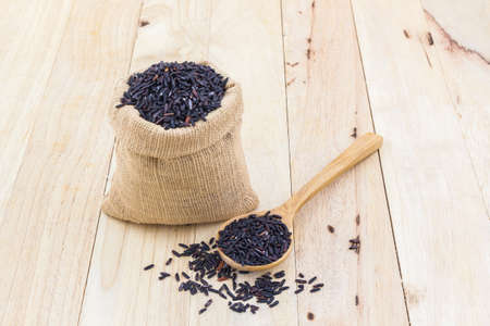 Rice berry in a wooden spoon and small burlap sack on wood background.の写真素材