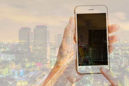 Double exposure of woman using her smart phone and city skyline night light background for...