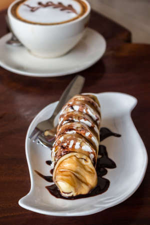 Banana crepe roll and with chocolate sauce on wooden table.の写真素材