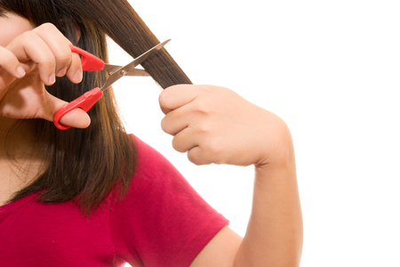 woman cutting her hair with scissors - unhappy expression, isolated on white backgroundの写真素材
