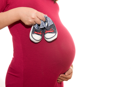Small shoes for the unborn baby in the belly of pregnant woman isolated on whiteの写真素材