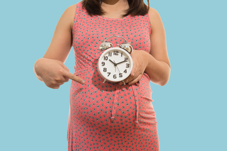 Pregnant woman holding  clock. It's time. on blue background soft colorの写真素材