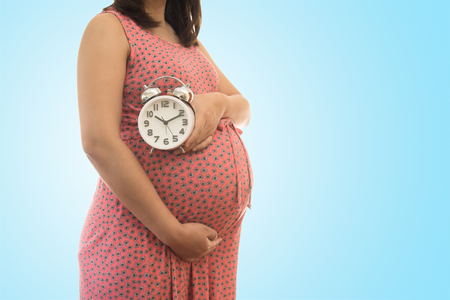 Pregnant woman holding  clock. It's time. on blue background soft colorの写真素材