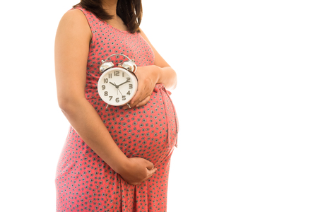 Pregnant woman holding wall clock. It's time. Isolated on white.の写真素材