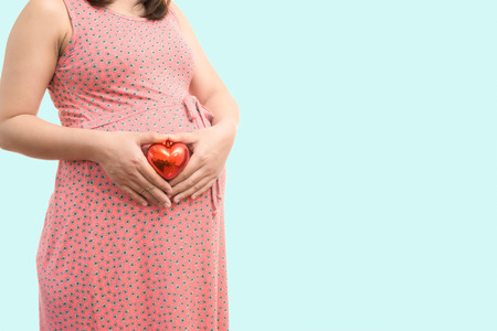 Pregnant woman belly holding gift heart. Healthy pregnancy isolate on blue backgroundの写真素材