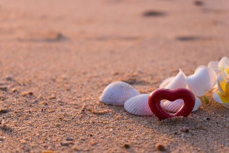 Group of frangipani, plumeria flowers, together with two red hearts, on sandの写真素材