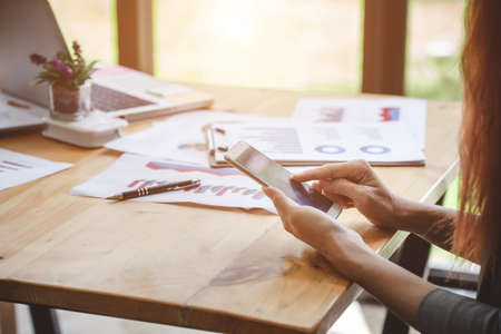 Business woman at working with financial reports and using mobile smartphone in the officeの写真素材