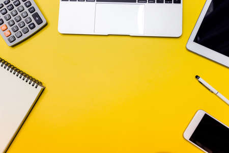 Yellow office desk table with  blank notebook, tablet, calculator and other office supplies. Top...
