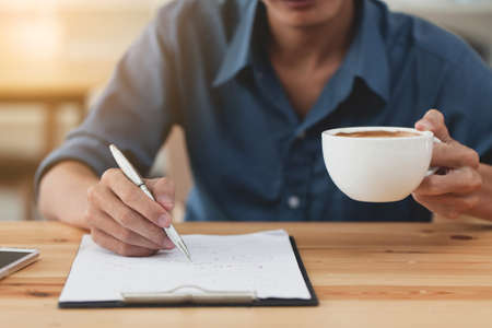 Business man writing note and drink coffee at home office.