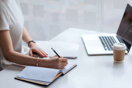 Close up. Woman hand taking notes with laptop at home.