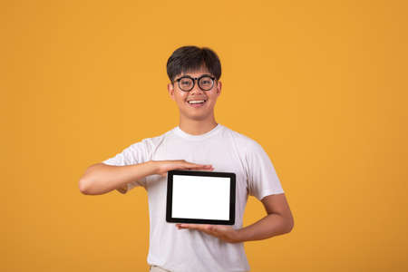 Asian man hold a tablet on a blank screen on orange background. Mock up.