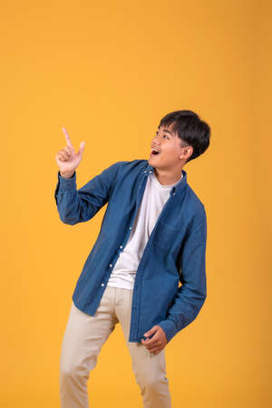 Asian man pointing his finger to look up. On orange backgroundの写真素材