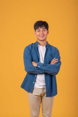 Young Asian man standing flat looking at the camera, with his hands crossed on an orange background.の写真素材