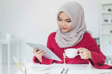 Young asian muslim woman using tablet and drinking coffee in the white coffee shop.の写真素材