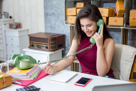 Smiling young entrepreneur woman talking on the telephone and write address to deliver the parcel to the customer.の写真素材