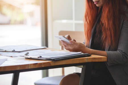 Business woman at working with financial reports and using mobile smartphone in the officeの写真素材