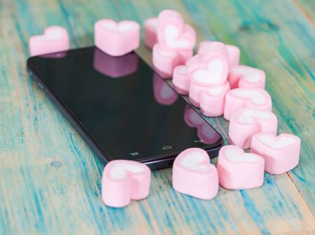 heart shape of marshmallows with smart phone on 
wood.selective focus.の写真素材