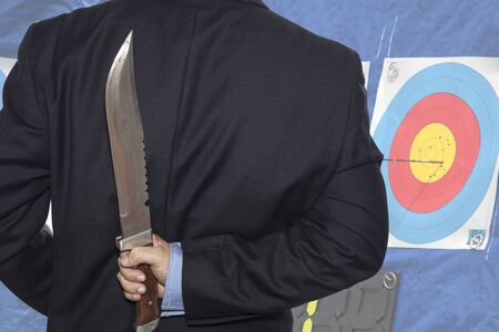 Knife hidden behind the businessman and target archery background.