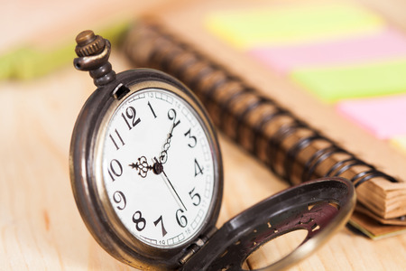 pocket watch with book note on wooden background.