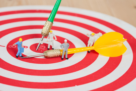 Miniature worker toy on red dart board with yellow dart arrowの写真素材