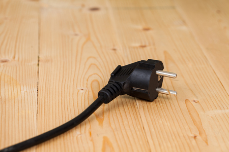 Hand holding a black electric plug on woodの写真素材