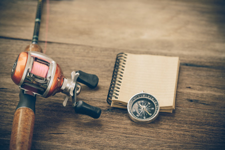 Fishing tackle - Baitcasting Reel, book and compass 
on  wooden backgroundの写真素材