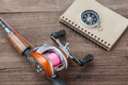Fishing tackle - Baitcasting Reel, book and compass on  wooden backgroundの写真素材