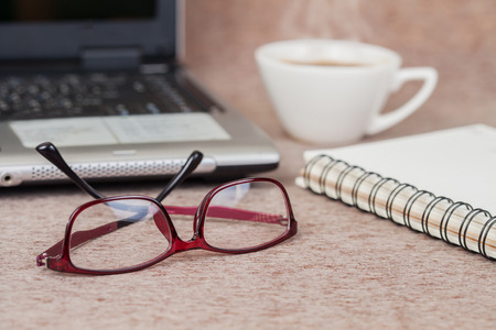 Selective focus office table : eyeglass , laptop, note book and cup on the woodenの写真素材