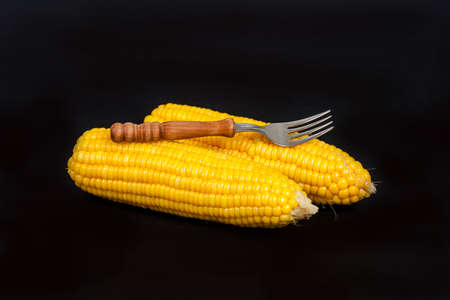 yellow fresh corn with fork on black backgroundの写真素材