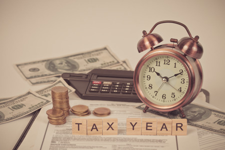 wording tax and calculator with tax documents, money and alarm clock on table. Tax concept.