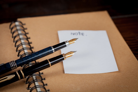 Two vintage fountain pens over a dairy book on wood table.の写真素材