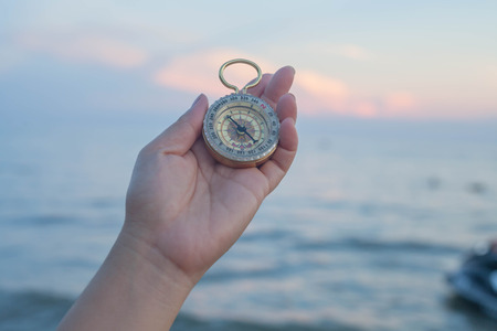 pocket compass in hand with sea background.