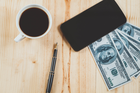 mobile on bank note with fountain pen and hot coffee on wood table.business concept.の写真素材