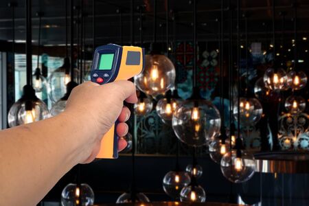 Yellow Infrared thermometer gun in hand used to measure temperature  on background.