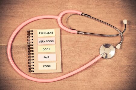 Pink stethoscope with healthcare level on paper note over wood table.の写真素材