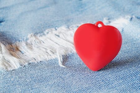 Red heart  laying on top of old and tear blue jeans. Valentine concept.