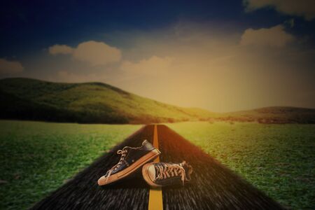 Old sneaker shoe on asphalt country road and landscape.の写真素材