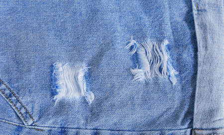 Tear of denim texture with a hole and threads showing.