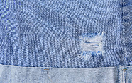 Tear of denim texture with a hole and threads showing.
