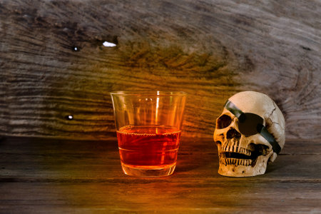 The pirate skull with a glass of rum liquor on brown wooden background.の写真素材