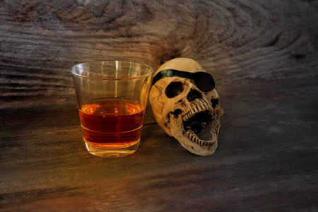 The skull with a glass of rum liquor on brown wooden background.の写真素材