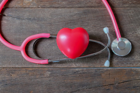 Red heart and a pink stethoscope on wood table.の写真素材