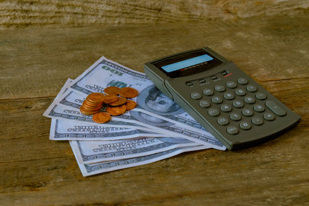 Calculator on US money and coins on table.の写真素材
