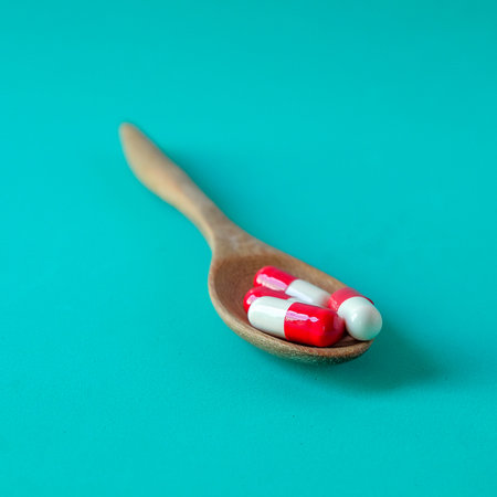 Medicine pills on wooden spoon over color background.の写真素材