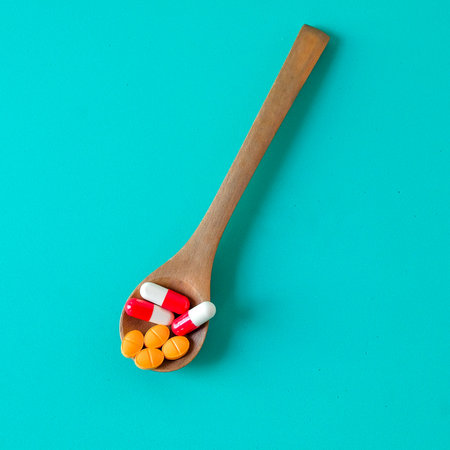Medicine pills on wooden spoon over color background.の写真素材