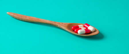 Medicine pills on wooden spoon over color background.の写真素材
