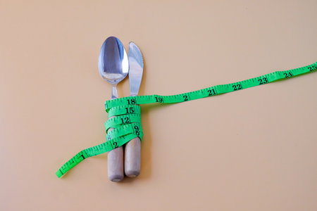 Green Measuring tape on a spoon and fork on color background.
