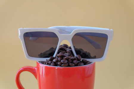 Coffee beans spill out of cup and sunglasses on color background.の写真素材