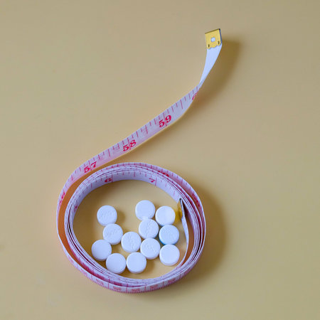 A measuring tape and diet pills lying on color background.