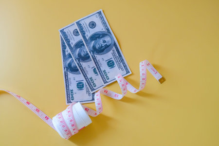 A measuring tape and diet pills with bank note lying on color background.